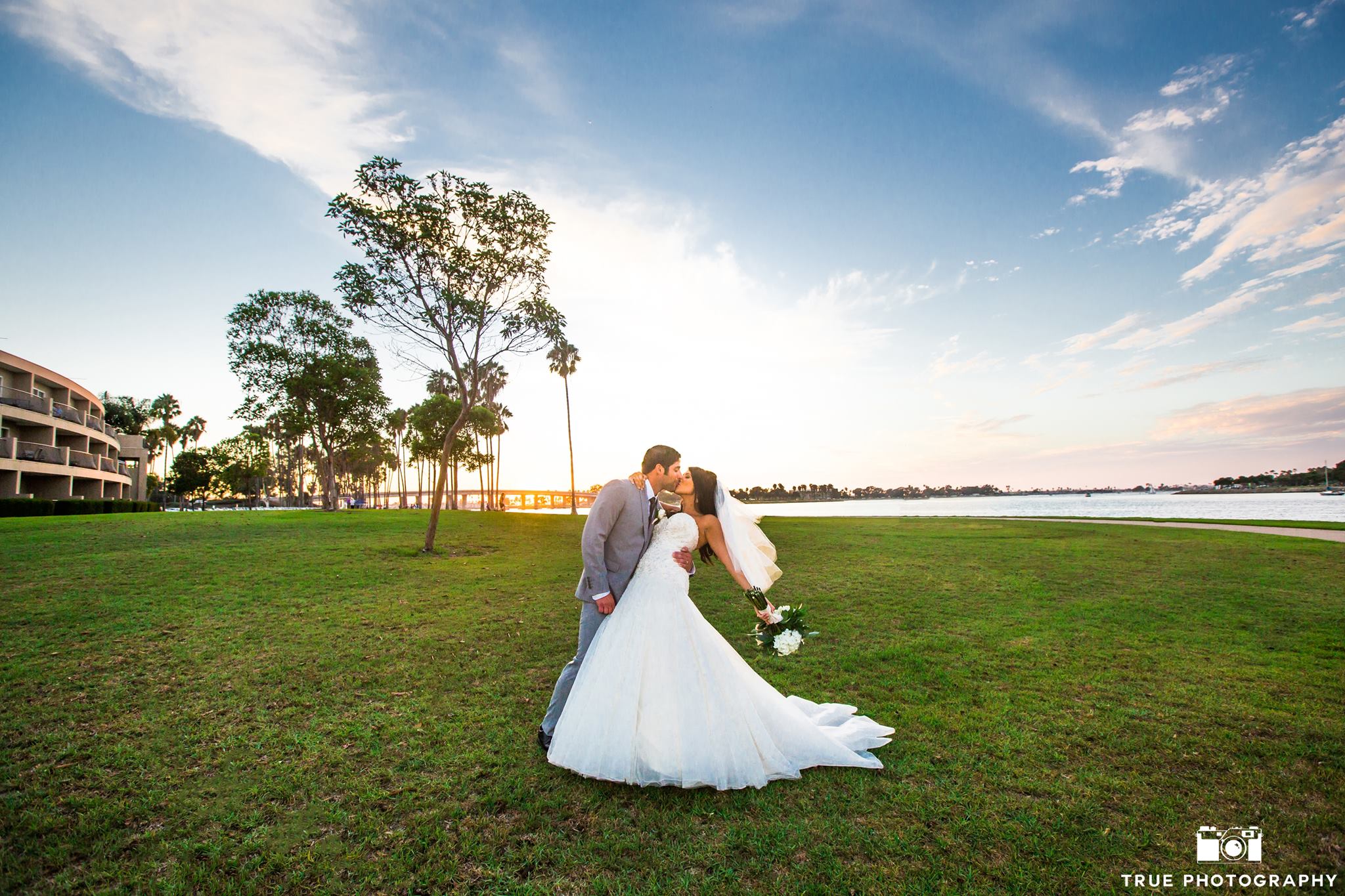 Bride and groom kiss on a waterfront lawn