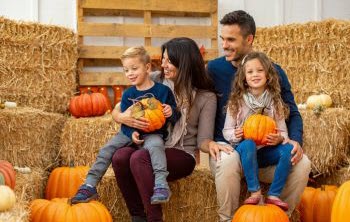 Family sitting on hay barrels and holding pumpkins