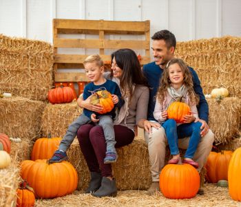 Family siting on hay barrels holding pumpkins