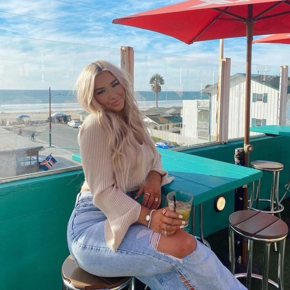 blond woman sitting on a rooftop patio with a red umbrella