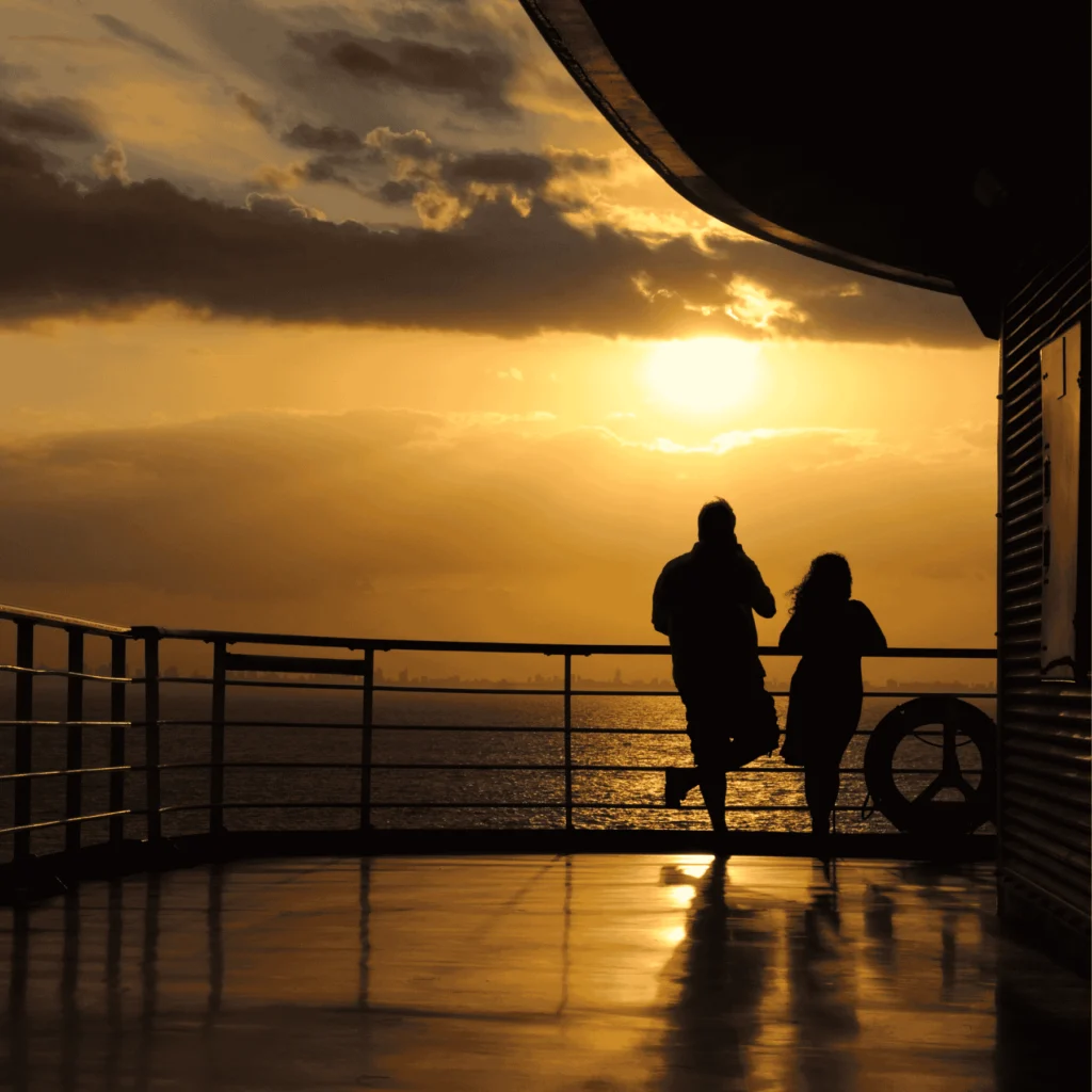 Two people standing on a cruise deck at sunset