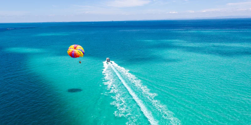 A boat in the water pulling a person parasailing.