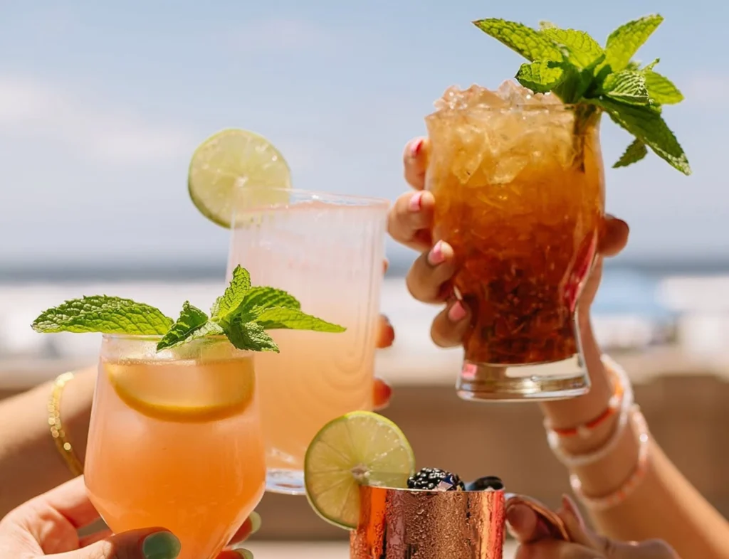 people holding cocktails in front of beach