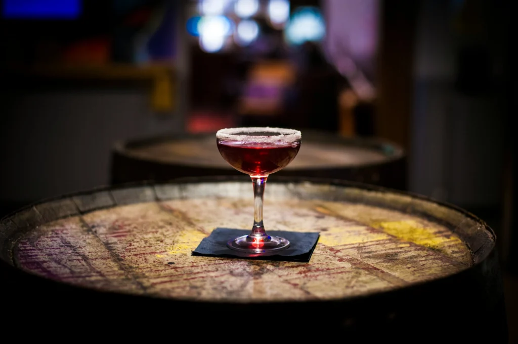 a red cocktail on a barrel in a low lit room